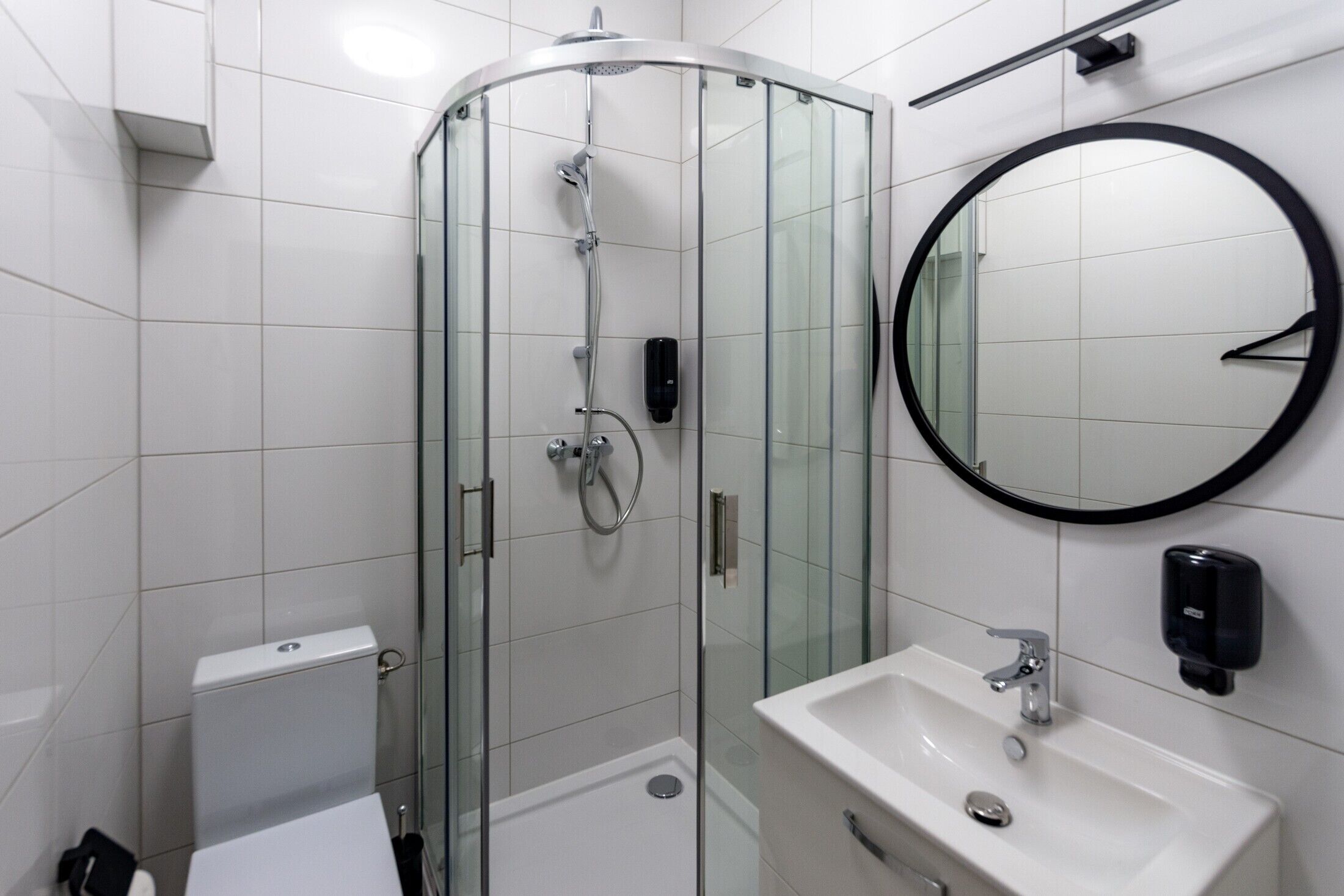 A modern bathroom with a glass-enclosed shower, a round mirror, and a white sink.