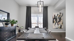 A dining room with a long table, dark wooden cabinets, a chandelier, and a large abstract painting on the wall. - Flexible Relocation Stay: Spacious, Pet-Friendly, w/ Utilities near Mid/Downtown (Atlanta)