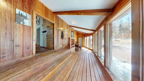 A wooden interior with a covered porch, wooden walls, and a view of the outdoors. - Large Deck | Fireplace | Forest Views | Kings Landing (Angel Fire)