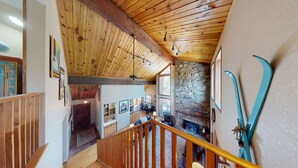A wooden interior with a stone wall, a staircase, and ski equipment. - Large Deck | Fireplace | Forest Views | Kings Landing (Angel Fire)