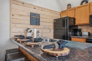 Une cuisine avec des murs recouverts de panneaux en bois, un évier en acier inoxydable, un réfrigérateur noir et un plan de travail en granit.