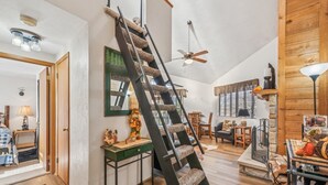 Un vaste espace de vie agrémenté d’un escalier en bois, d’un ventilateur de plafond et d’une cheminée.