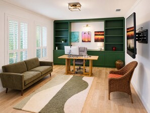 Une pièce avec un mur vert, un bureau avec un ordinateur, un canapé, une chaise et des œuvres d’art.