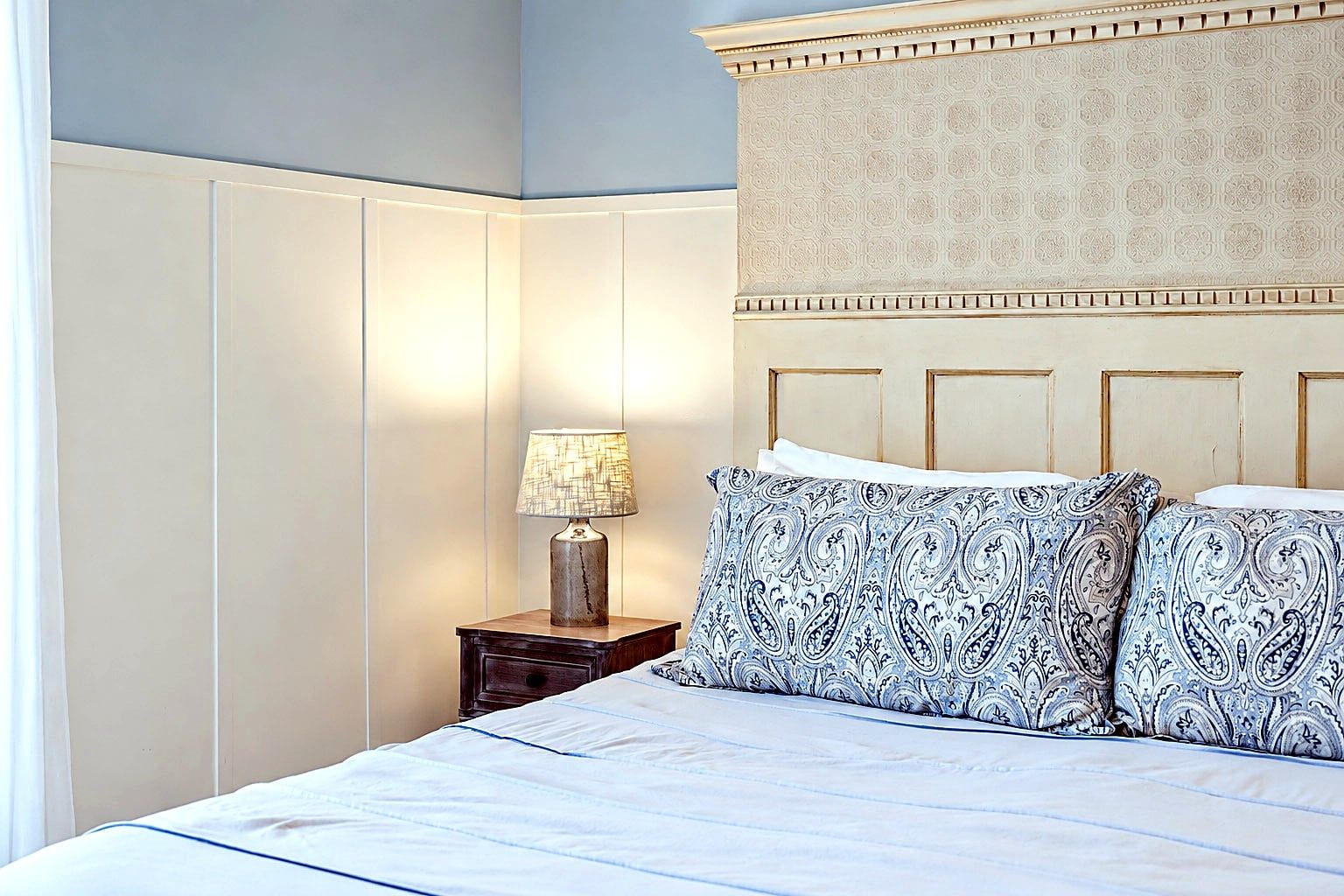 A bedroom with a bed, a nightstand with a lamp, and a patterned headboard.