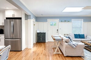 A modern kitchen with a stainless steel refrigerator, wooden flooring, and a dining area with a white table and chairs.