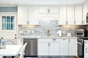 A modern kitchen with white cabinetry, a brick backsplash, and stainless steel appliances.