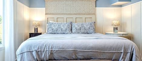 A bedroom with a large bed, two bedside tables with lamps, a headboard, and a bench at the foot of the bed.