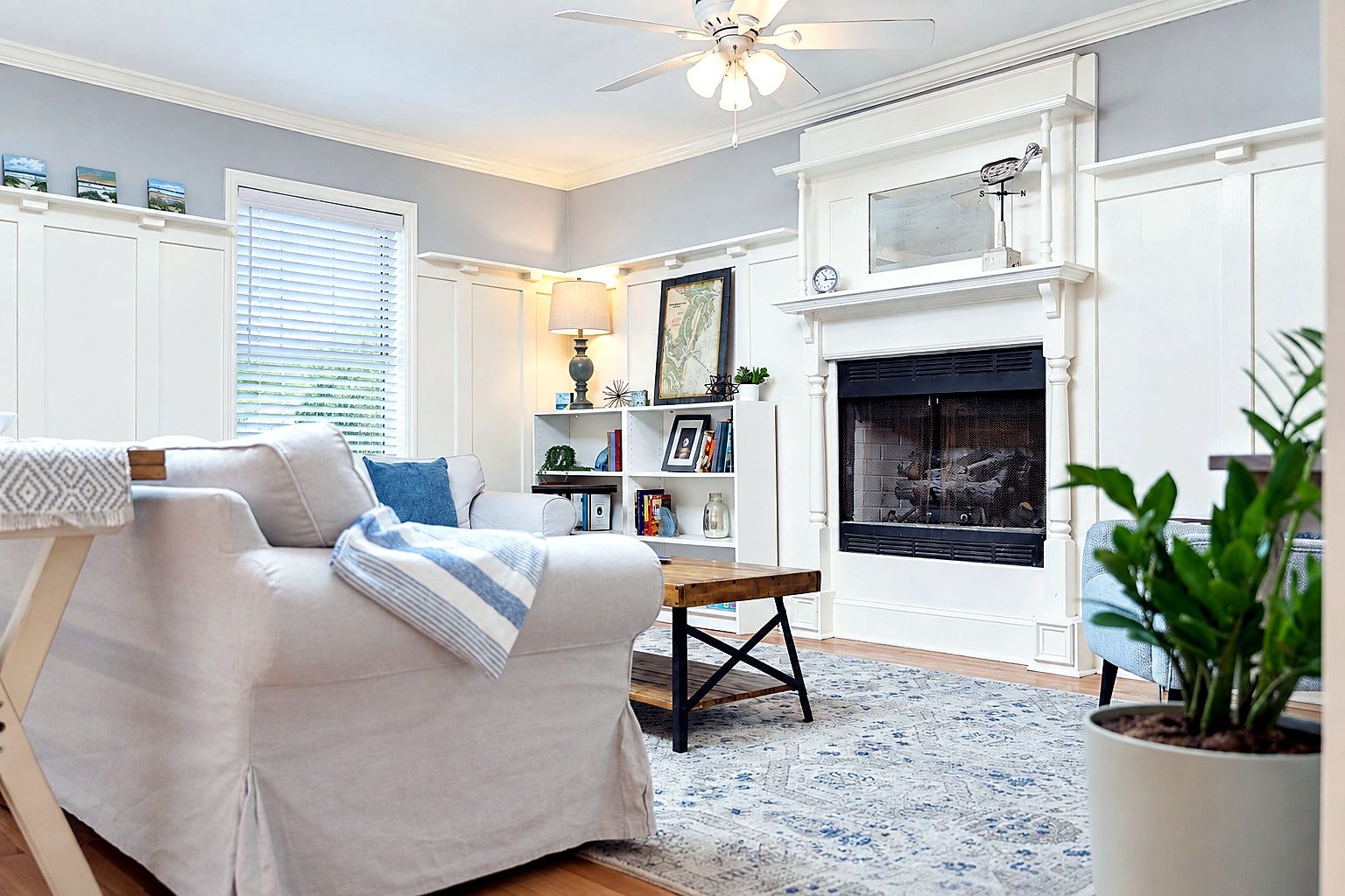 A living room with a white sofa, a fireplace, a ceiling fan, and a bookshelf.