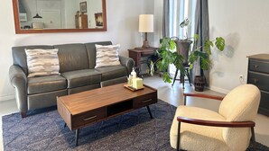 Un salon comprenant un canapé, une table basse, un fauteuil, une plante en pot et un grand miroir.