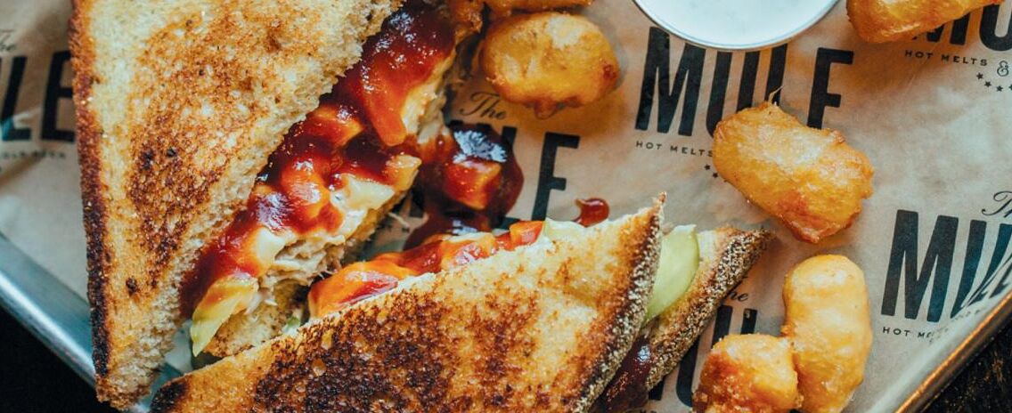 A grilled sandwich with a side of fries and a small container of sauce.