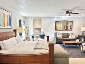 A hotel room with a large bed, a sofa, a desk, a chair, a ceiling fan, a mirror, and a plant. - Modern Studio Retreat Stylish Spacious MR (Oklahoma City)