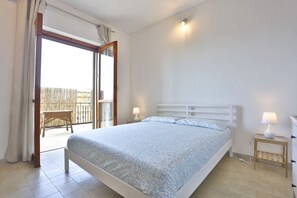 A bedroom with a bed, a nightstand, a lamp, a window, and a door leading to an outdoor area.