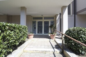 L'ingresso di un edificio con un vialetto lastricato, piante in vaso e una ringhiera in metallo.