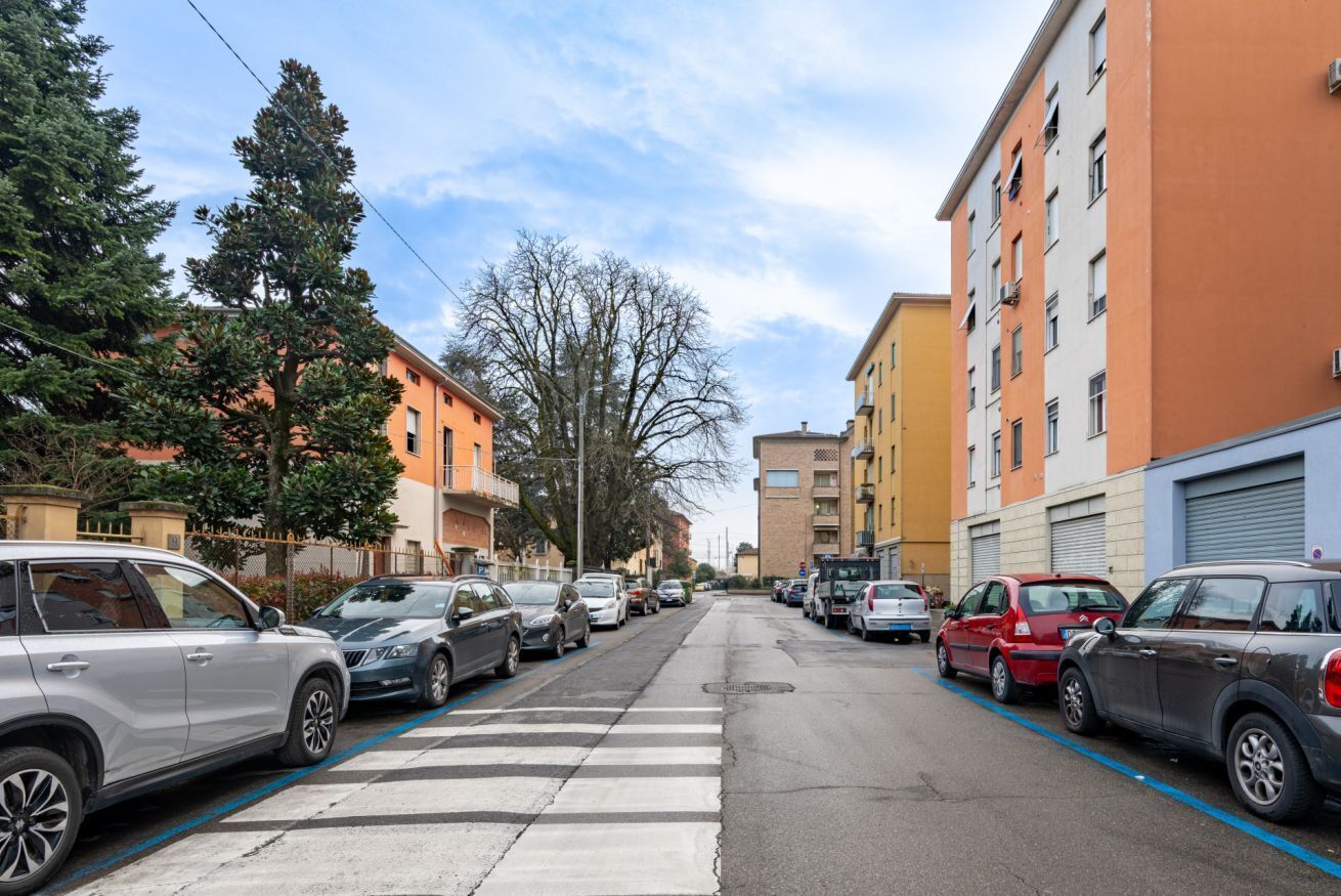 Una calle con automóviles estacionados, edificios y un paso de cebra.
