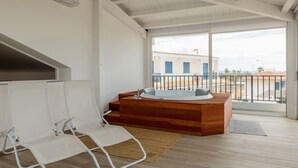 Ein modernes Badezimmer mit einer Holzwanne, weißen Stühlen und einem großen Fenster mit Blick auf Gebäude.