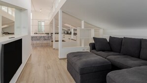 Ein modernes Wohnzimmer mit einer Eckcouch, einem Flachbildfernseher und einer Küche im Hintergrund.