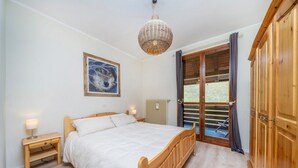 Een slaapkamer met een houten bed, een nachtkastje, een wandlamp, een schilderij en een raam met gordijnen.