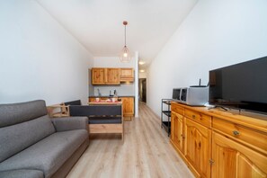 Un salon moderne avec un canapé gris, des meubles en bois, un téléviseur et une cuisine en arrière-plan.