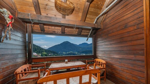 Een houten chalet met een tafel en stoelen, een raam met uitzicht op de bergen, en een hangmand.