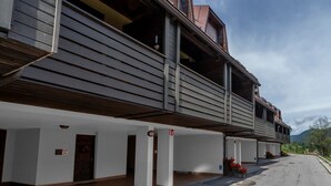 Een gebouw met een overdekt terras, een houten balkon en een bord dat een vluchtweg aangeeft.