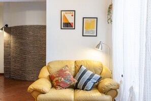 Une pièce avec un canapé en cuir jaune, deux coussins, une lampe fixée au mur et deux affiches encadrées.