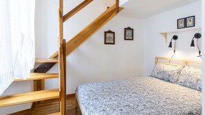 Ein Schlafzimmer mit einer Holztreppe, einem Bett mit gemusterten Textilien und Wandleuchten.
