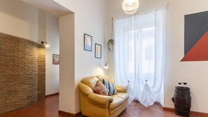 Ein Zimmer mit einer Couch, einer Holzwand, einem Fenster mit Vorhängen und einem Fass.