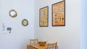 Ein Essbereich mit einem Holztisch, zwei Stühlen, einer Obstschale und zwei gerahmten Postern an der Wand.