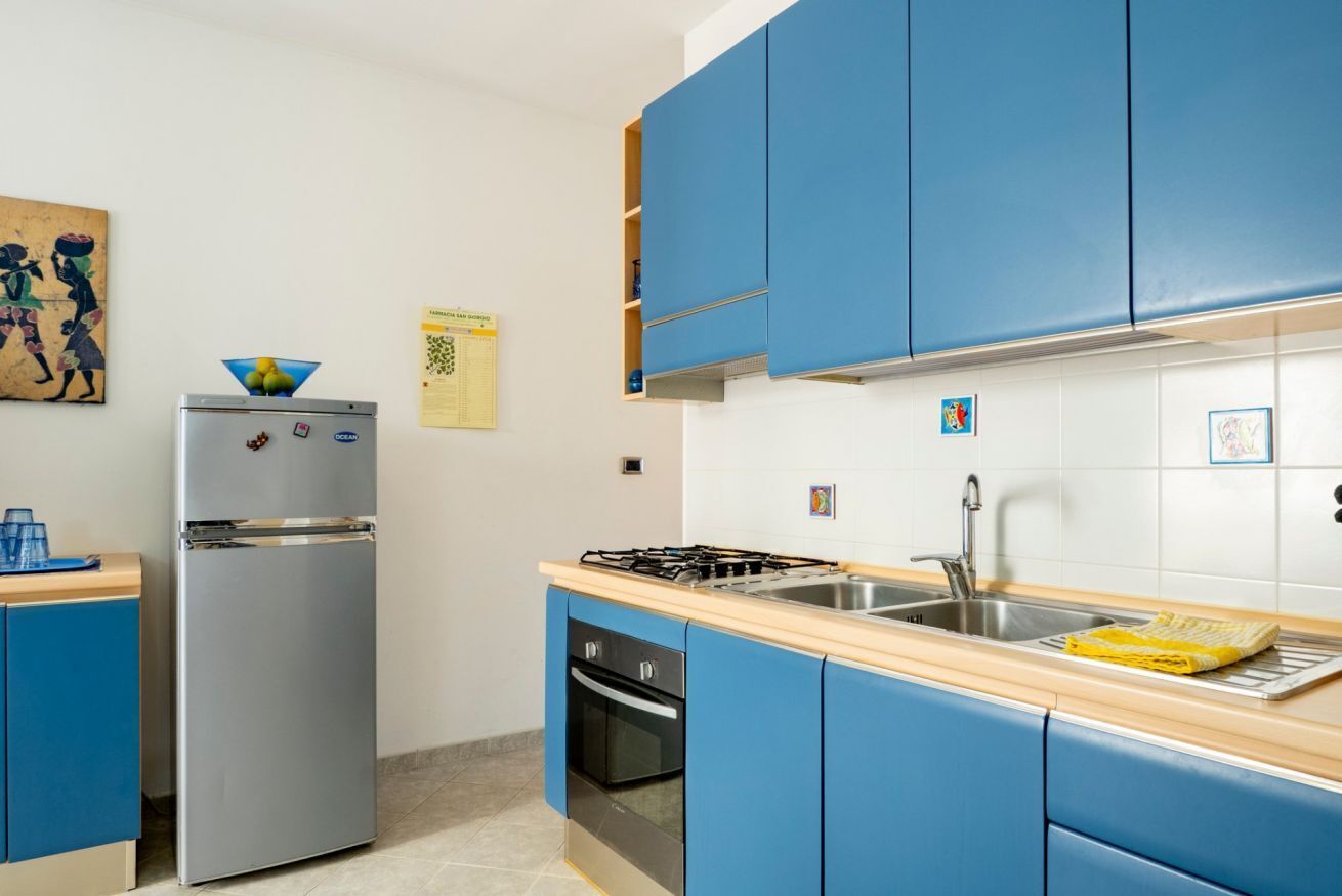 A kitchen with blue cabinets, a stainless steel refrigerator, a gas stove, and a sink.