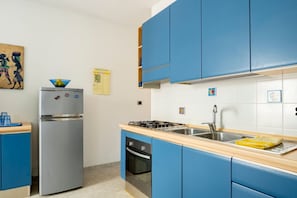 A kitchen with blue cabinets, a stainless steel refrigerator, a gas stove, and a sink.