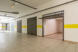 Un espacio interior amplio con pisos de baldosas, un techo alto con tuberías a la vista y una franja amarilla en las paredes.