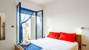 Un dormitorio con cama, ventana con cortinas, mesita de noche y lámpara.