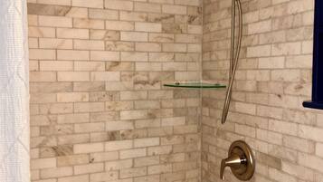 Ein Badezimmer mit einer weißen Badewanne, einer Glasablage und einer Dusche inklusive Duschbrause.