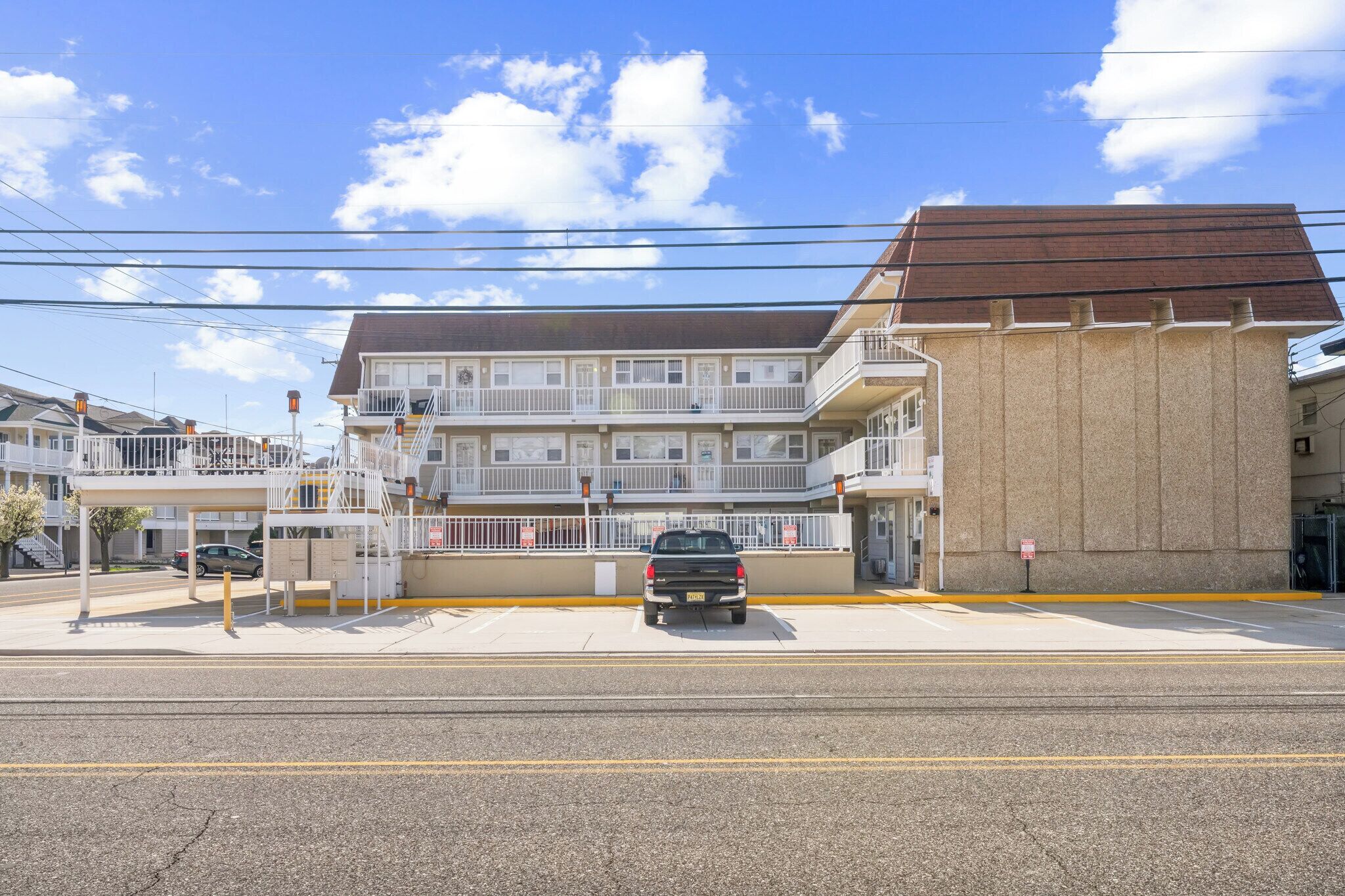 A multi-story hotel with a balcony on the second floor, a parking lot, and a clear sky.