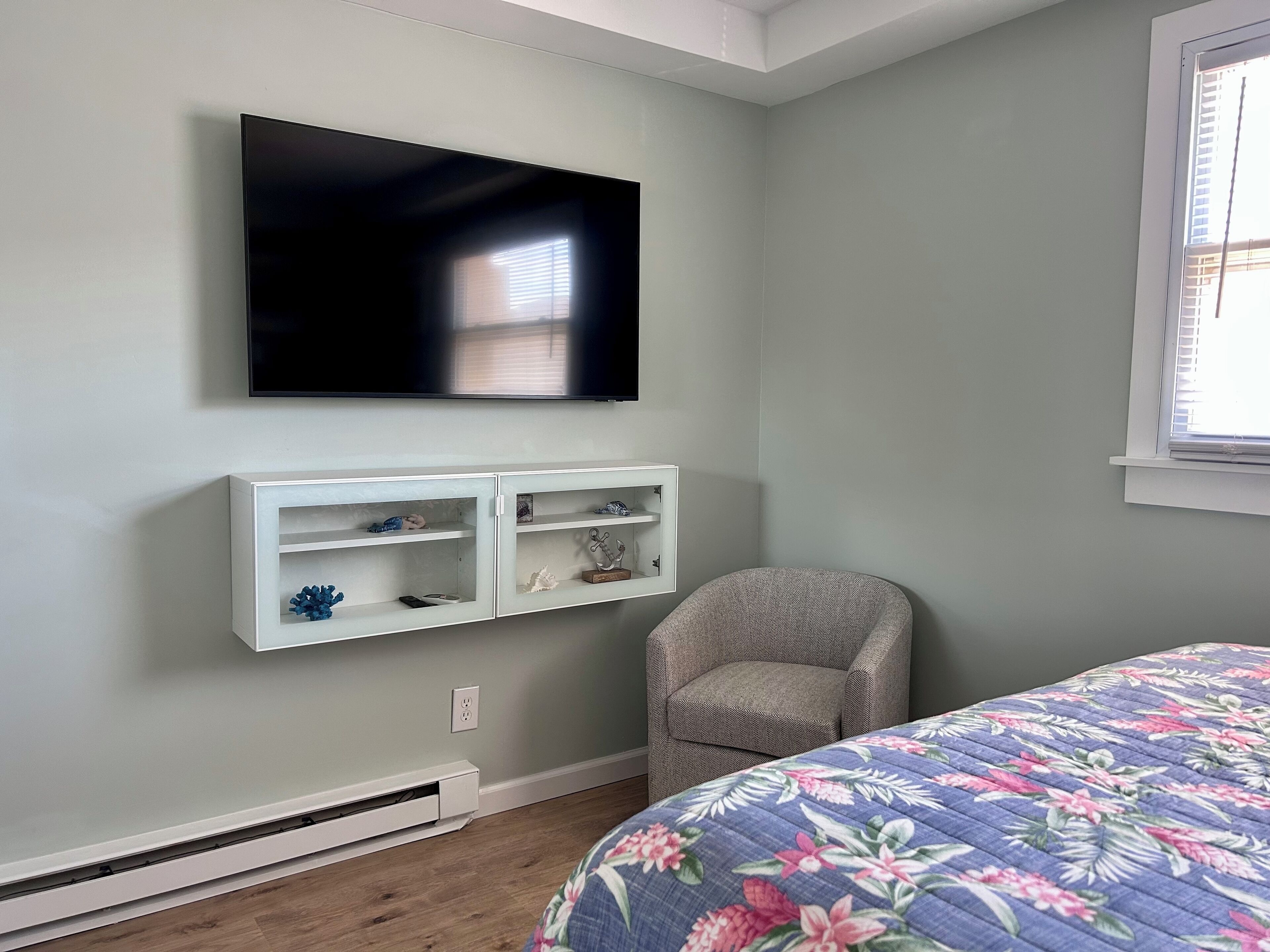 Una camera da letto con un letto, una TV a parete, una sedia e una finestra.