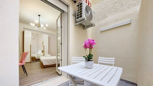 Una habitación pequeña con una cama, una mesa blanca con una planta en maceta y una silla blanca.