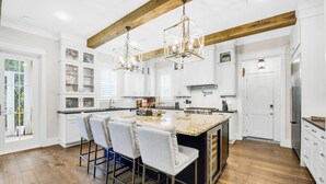 Un'ampia cucina con un'isola grande, travi in legno, mobili bianchi e un lampadario moderno.