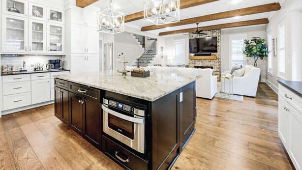 Un'ampia cucina con una grande isola, travi in legno e un moderno lampadario.