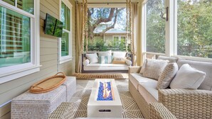 Un portico baciato dal sole, con mobili in vimini, un elemento decorativo a forma di fuoco e vista su un albero e una casa sullo sfondo.
