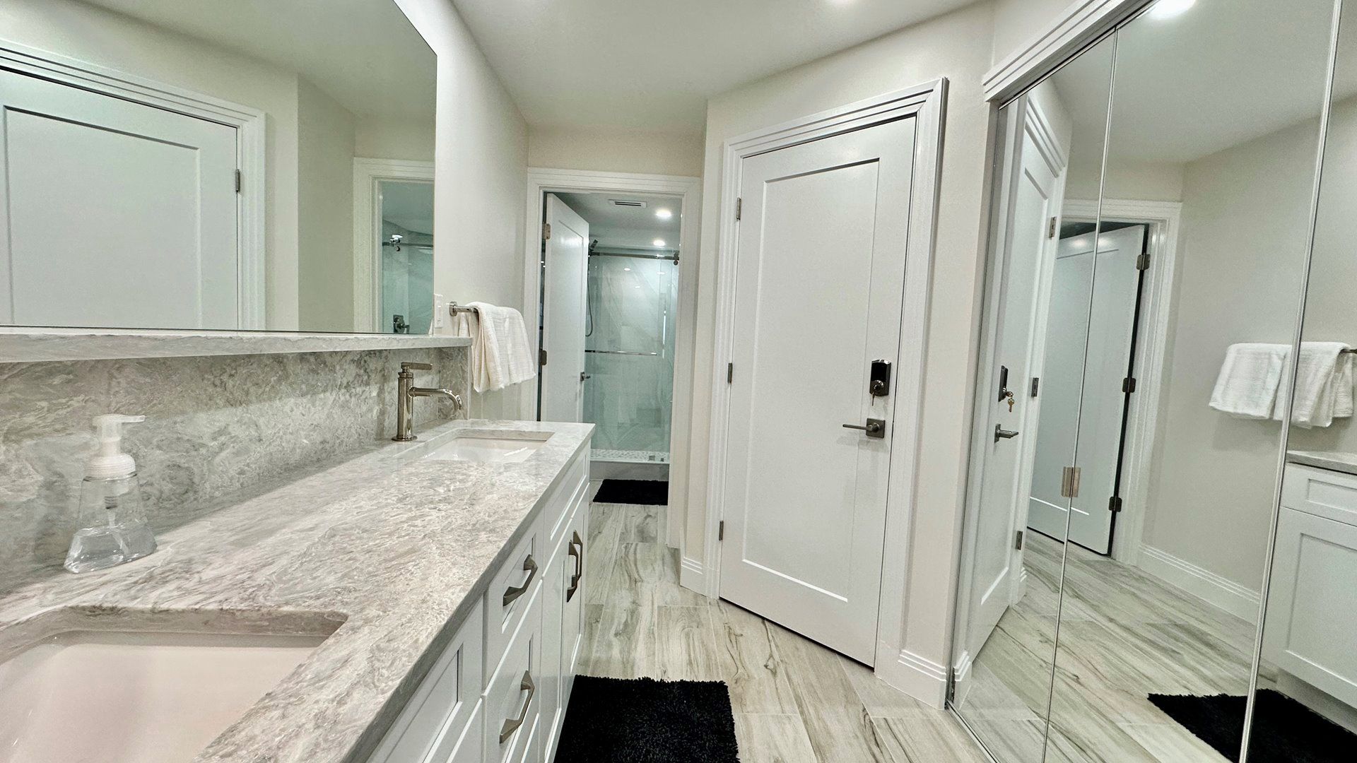 A modern bathroom with a marble countertop, a glass shower enclosure, and a walk-in closet with mirrored doors.