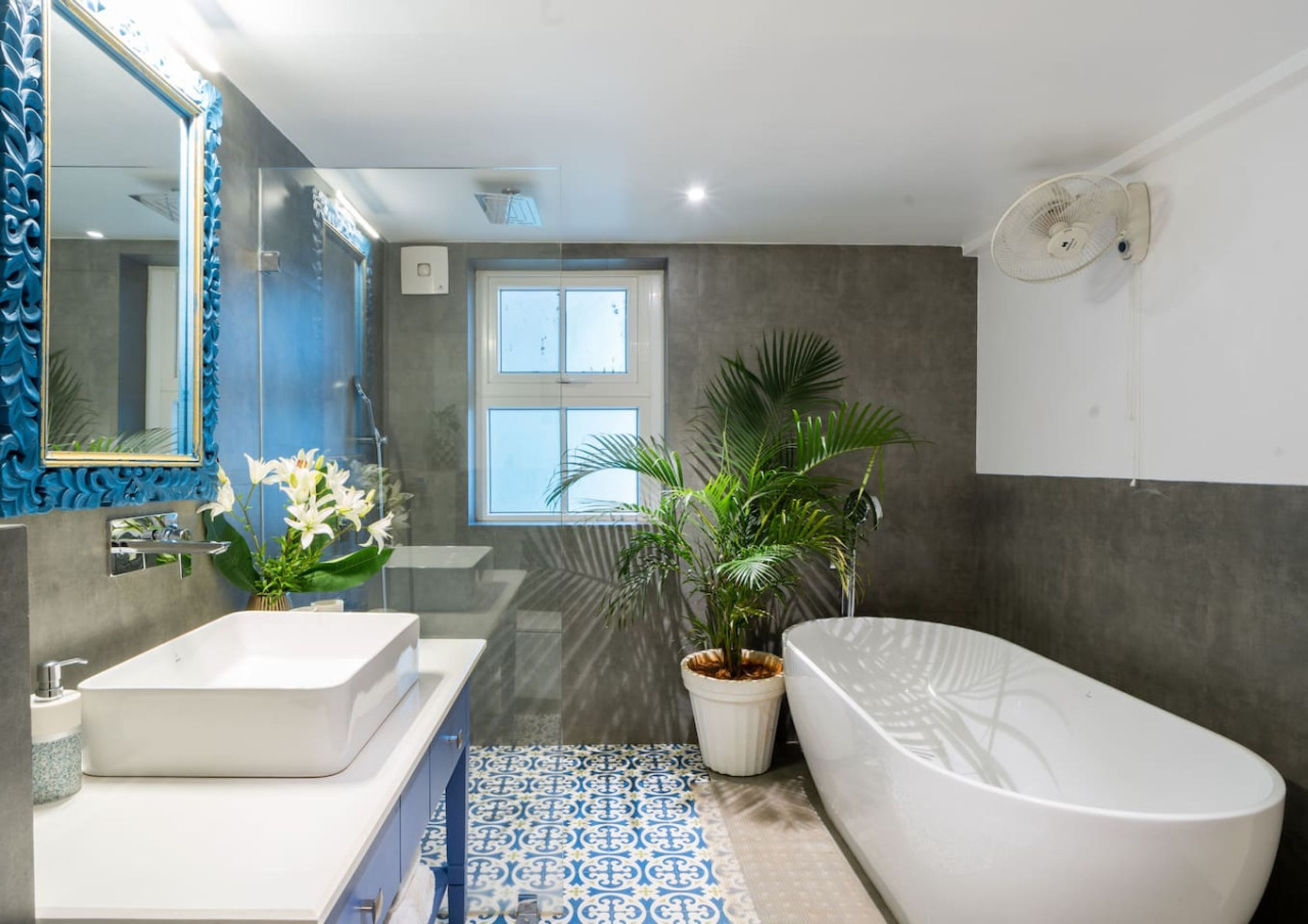A modern bathroom with a large mirror, two sinks, a bathtub, and a window.