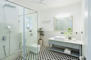 A modern bathroom with a glass shower enclosure, a white sink, a mirror, and a patterned floor.