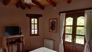 A bedroom with a bed, a television on a wooden stand, a window with curtains, and a painting on the wall. - Complejo Turístico Cruz Mendoza (Tilcara)