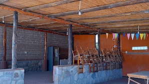 A covered outdoor area with a thatched roof, stone walls, and a seating area with wooden benches. - Complejo Turístico Cruz Mendoza (Tilcara)