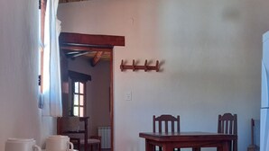 A dining area with a wooden table and chairs, a hanging light fixture, and a wall-mounted coat rack. - Complejo Turístico Cruz Mendoza (Tilcara)