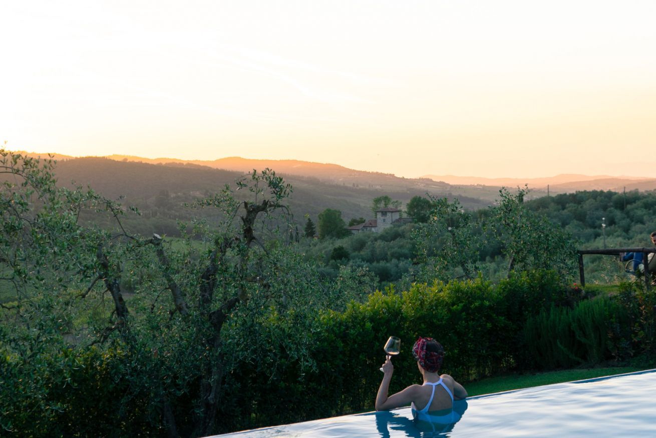 Una persona descansando en una piscina con vistas panorámicas a colinas y viñedos.