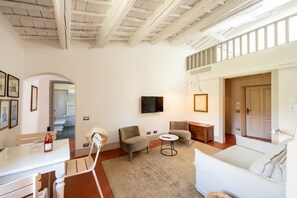 A spacious living room with a high ceiling, a flat-screen TV mounted on the wall, a sofa, two armchairs, a small round table, and a dining table with chairs. - Unique Villa with Infinity Pool in the heart of Chianti (Greve in Chianti)