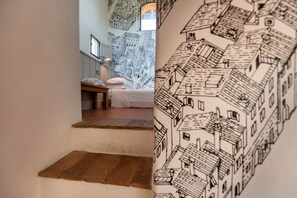 Une chambre avec un lit, une table de chevet et un mur orné d’un dessin en noir et blanc représentant un paysage urbain.