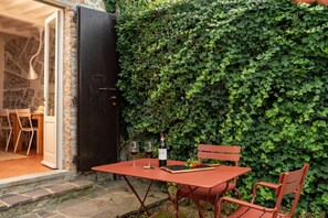 An outdoor dining area with a table and chairs, a bottle of wine, and glasses on a table.