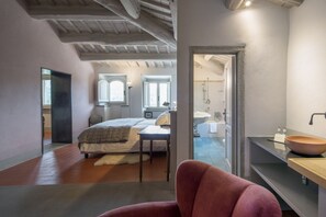 A bedroom with a bed, a chair, a mirror, and a bathroom visible through an open door. - Unique Villa with Infinity Pool in the heart of Chianti (Greve in Chianti)